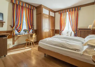 a bedroom with a bed and a desk and two windows at Parc Hotel Victoria in Cortina dʼAmpezzo