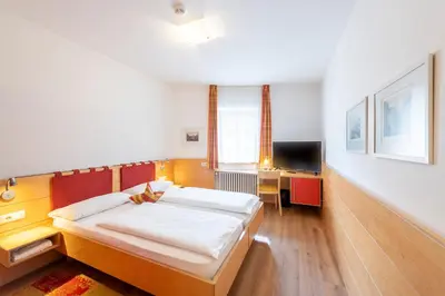 a bedroom with two beds and a desk and a television at Hotel Figl ***S in Bolzano