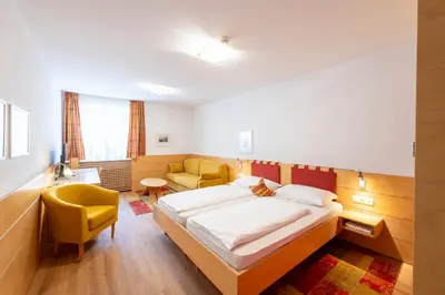 a bedroom with a large bed and a yellow chair at Hotel Figl ***S in Bolzano