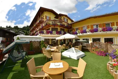 an outdoor patio with tables and chairs and a building at Hotel Alle Alpi in Moena