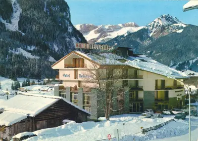a building in the snow with mountains in the background at Hotel Bellevue in Canazei