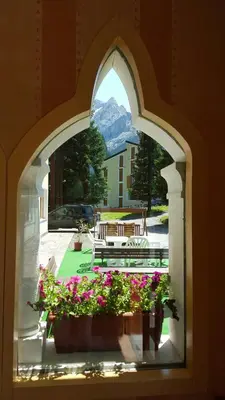 an arched window with a view of a patio with flowers at IHR Hotel Villa Emma in Canazei
