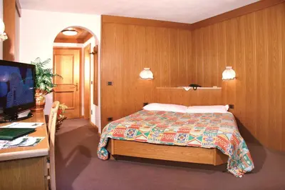 a bedroom with a bed and a desk and a television at Hotel Villetta Maria Cottage in Canazei