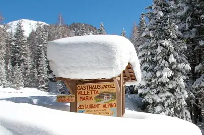 a sign covered in snow next to a tree at Hotel Villetta Maria Cottage in Canazei