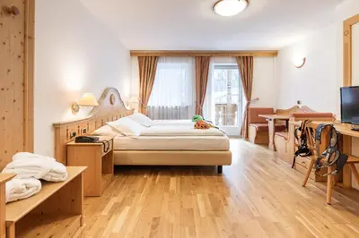 a bedroom with a bed and a desk and a television at Hotel Soreghes Gran Chalet in Campitello di Fassa