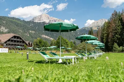 a row of lawn chairs with green umbrellas in a field at Hotel Diamant Park in Campitello di Fassa