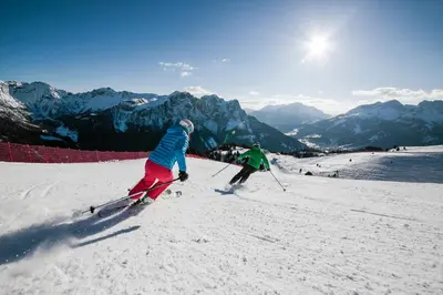two people are skiing down a snow covered slope at Hotel Diamant Park in Campitello di Fassa