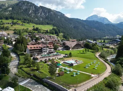 a large building in the snow in front of mountains at Hotel Rubino Deluxe in Campitello di Fassa