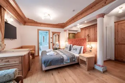 a bedroom with a bed and a desk and a tv at Hotel Grohmann in Campitello di Fassa