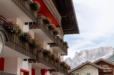 a building with flowers on the balconies with mountains in the background at Hotel Grohmann in Campitello di Fassa