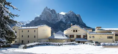 a building in the snow with a mountain in the background at Mirabell Alpine Garden Resort & Spa in Siusi