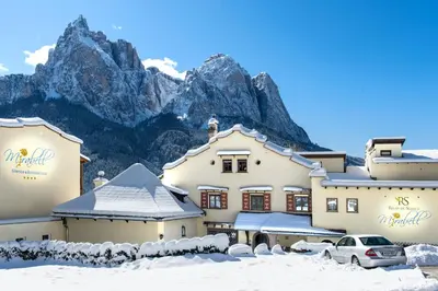 a hotel in the snow with mountains in the background at Mirabell Alpine Garden Resort & Spa in Siusi