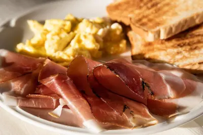 a plate of breakfast food with bacon eggs and toast at Hotel Medil in Campitello di Fassa