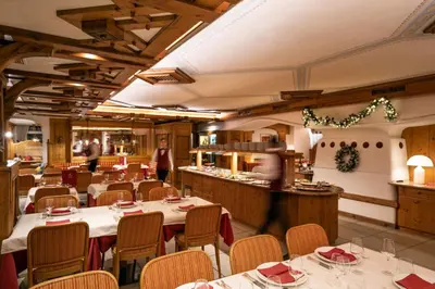 a restaurant with tables and chairs and a chef in the kitchen at Hotel Medil in Campitello di Fassa