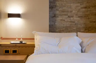 a bedroom with a bed with white sheets and a brick wall at Hotel Medil in Campitello di Fassa