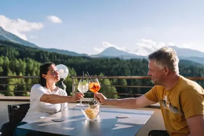 a man and woman sitting at a table with glasses of wine at Hotel Obereggen in Obereggen
