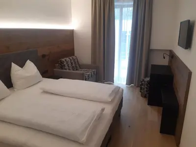 a bedroom with a white bed and a chair and a window at Hotel Krone in Brunico