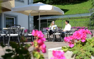 two people sitting at a table under an umbrella at Rio Stava Family Resort & Spa in Tesero