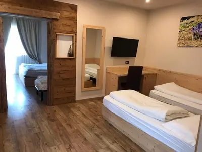 a room with three beds and a desk with a television at Park Hotel Avisio in Soraga