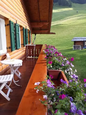 a wooden porch with flowers and a table and chairs at Garni Rubens B&B in Selva di Val Gardena