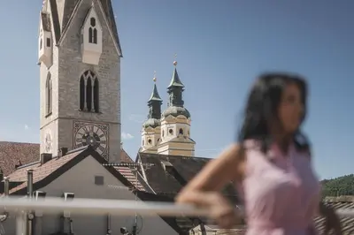a woman walking past a church with a clock tower at Residence Chiavi D'Oro - Goldener Schlüssel in Bressanone