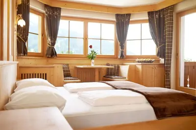 a bedroom with four beds in a room with windows at Garni Hotel Rosengarten B&B in Selva di Val Gardena