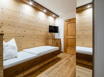 a bedroom with a wooden wall with two beds at Garni Hotel Rosengarten B&B in Selva di Val Gardena