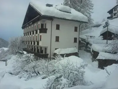 a building covered in snow with bushes and trees at Albergo Posta in Colle Santa Lucia