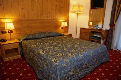 a hotel room with a bed and two tables and two lamps at GH Hotel Monzoni in Pozza di Fassa