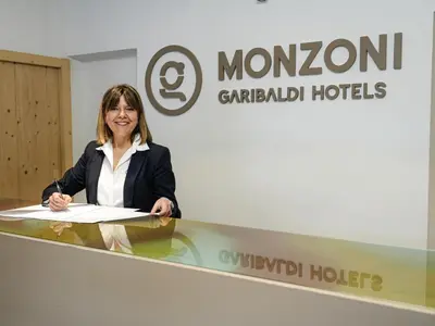 a woman standing behind a counter in front of a sign at GH Hotel Monzoni in Pozza di Fassa