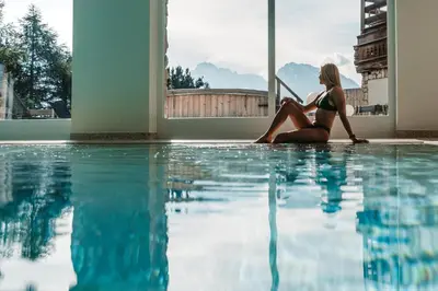 a woman in a bikini sitting next to a swimming pool at Paradiso Pure Living Vegan Hotel in Alpe di Siusi