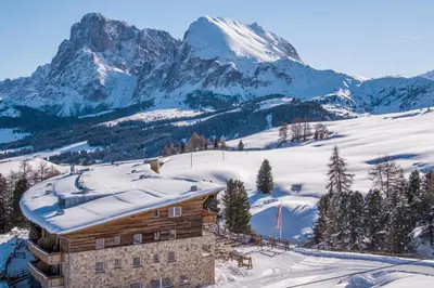 a building in the snow with mountains in the background at Paradiso Pure Living Vegan Hotel in Alpe di Siusi