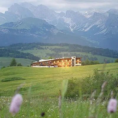 a building in a field with mountains in the background at Paradiso Pure Living Vegan Hotel in Alpe di Siusi