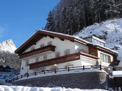 a building on a snow covered hill with a snow covered mountain at Villa Perla in Selva di Val Gardena
