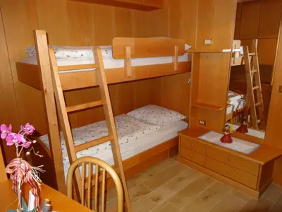 a bunk room with two bunk beds and a table at Villa Perla in Selva di Val Gardena