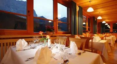 a dining room with white tables and chairs and windows at Hotel Meisules in Selva di Val Gardena