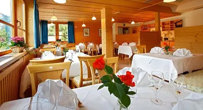 a restaurant with white tables and chairs with red flowers at Hotel Meisules in Selva di Val Gardena