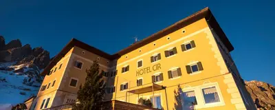 a yellow building with a mountain in the background at Hotel Cir in Selva di Val Gardena