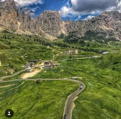 a farm in the mountains under a blue sky at Hotel Cir in Selva di Val Gardena