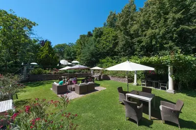 a garden with chairs and tables and umbrellas at Hotel Lambrechtshof in Appiano sulla Strada del Vino