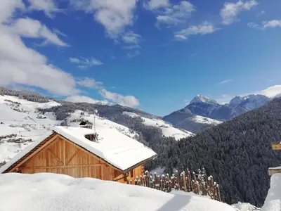 a wooden cabin in the snow with mountains in the background at Naturchalet in San Vigilio Di Marebbe