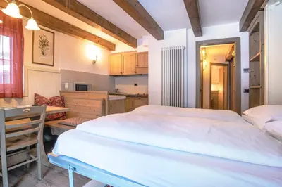 a bedroom with a bed and a desk and a kitchen at Al Sole Clubresidence in Canazei