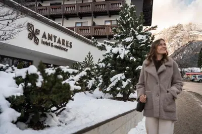 a woman standing in the snow in front of a building at Hotel Antares in Selva di Val Gardena