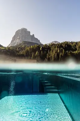 a pool of water with a mountain in the background at Hotel Touring Dolomites in Santa Cristina in Val Gardena