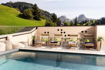 a pool at a resort with chairs and a table at Hotel Touring Dolomites in Santa Cristina in Val Gardena