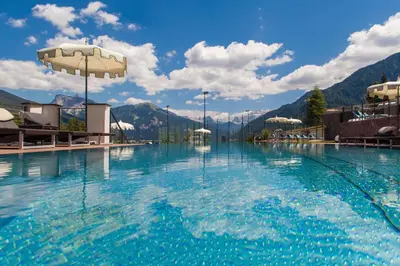 a large swimming pool with mountains in the background at Hotel Albion Mountain Spa Resort Dolomites in Ortisei