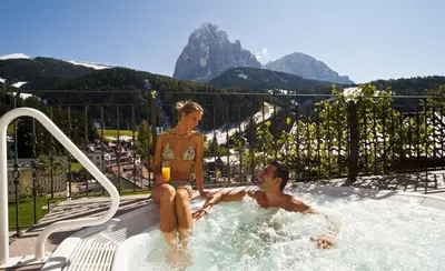 a man and a woman sitting in a swimming pool at Hotel Interski in Santa Cristina in Val Gardena