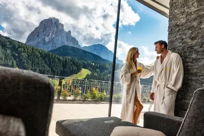 a man and woman standing on a balcony with a view of mountains at Hotel Interski in Santa Cristina in Val Gardena