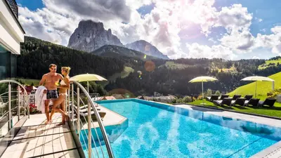 a man and woman sitting on the edge of a swimming pool at Hotel Interski in Santa Cristina in Val Gardena