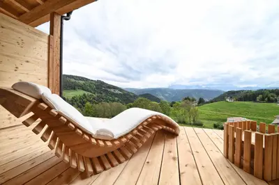 a wooden rocking chair on a deck with a view at Hotel & Gasthof zum Hirschen in San Genesio Atesino